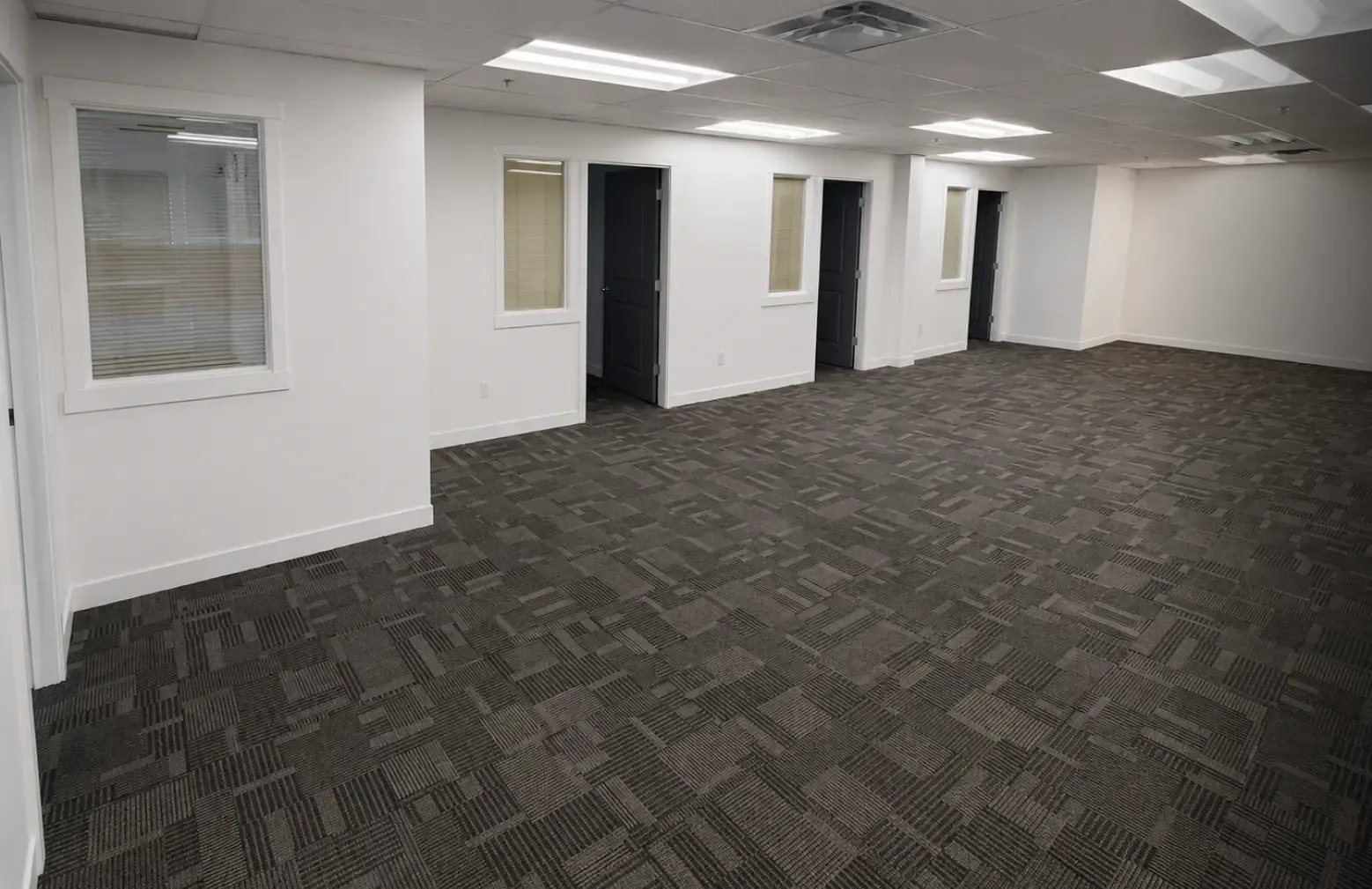 After photo of a fully remodeled open workspace commercial office by Pacific Coast Contracting, featuring new modular dark carpeting, finished drop ceilings, and bright white walls.